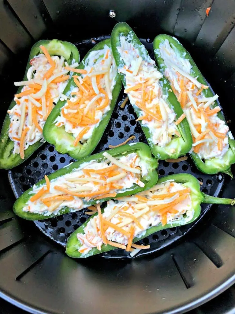 fresh jalapenos sliced in half on a cutting board stuffed with cheese in an air fryer