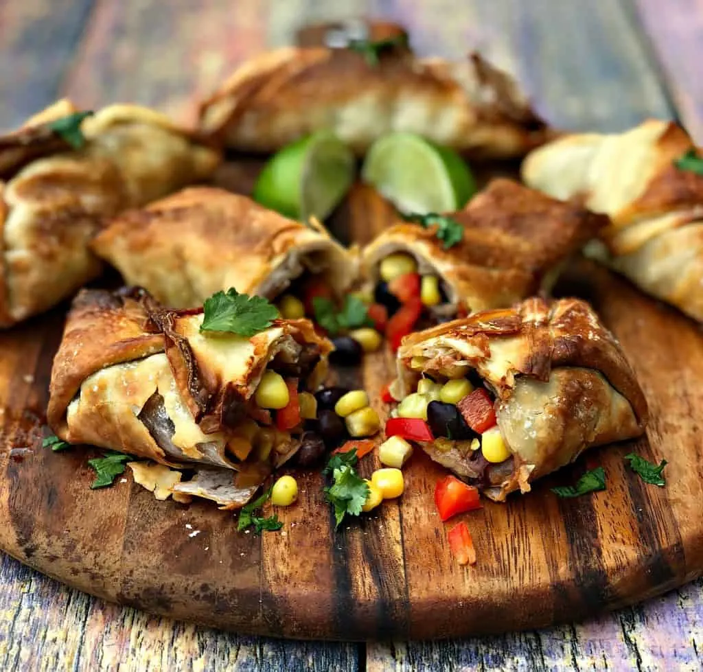 air fryer southwestern egg rolls cut in half with black beans, corn and red peppers spread out on a brown cutting board