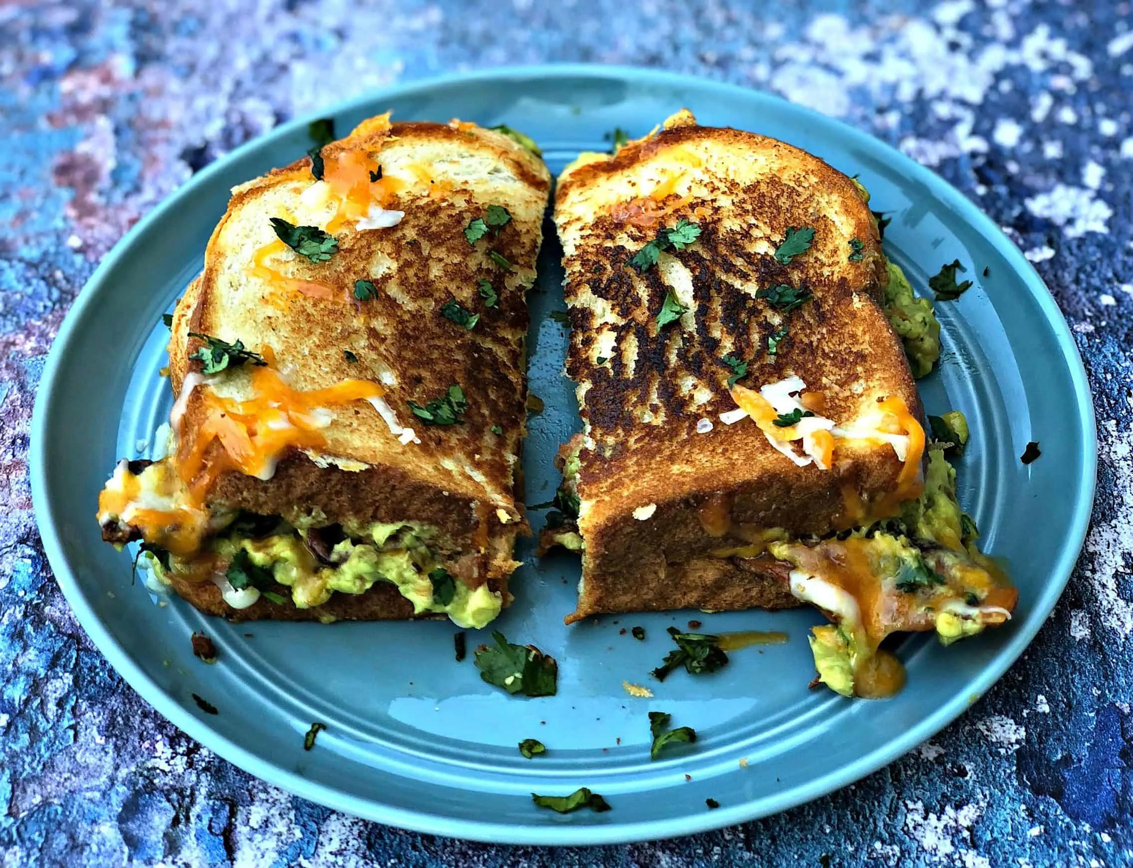 guacamole bacon grilled cheese sandwich cut in half on a blue plate