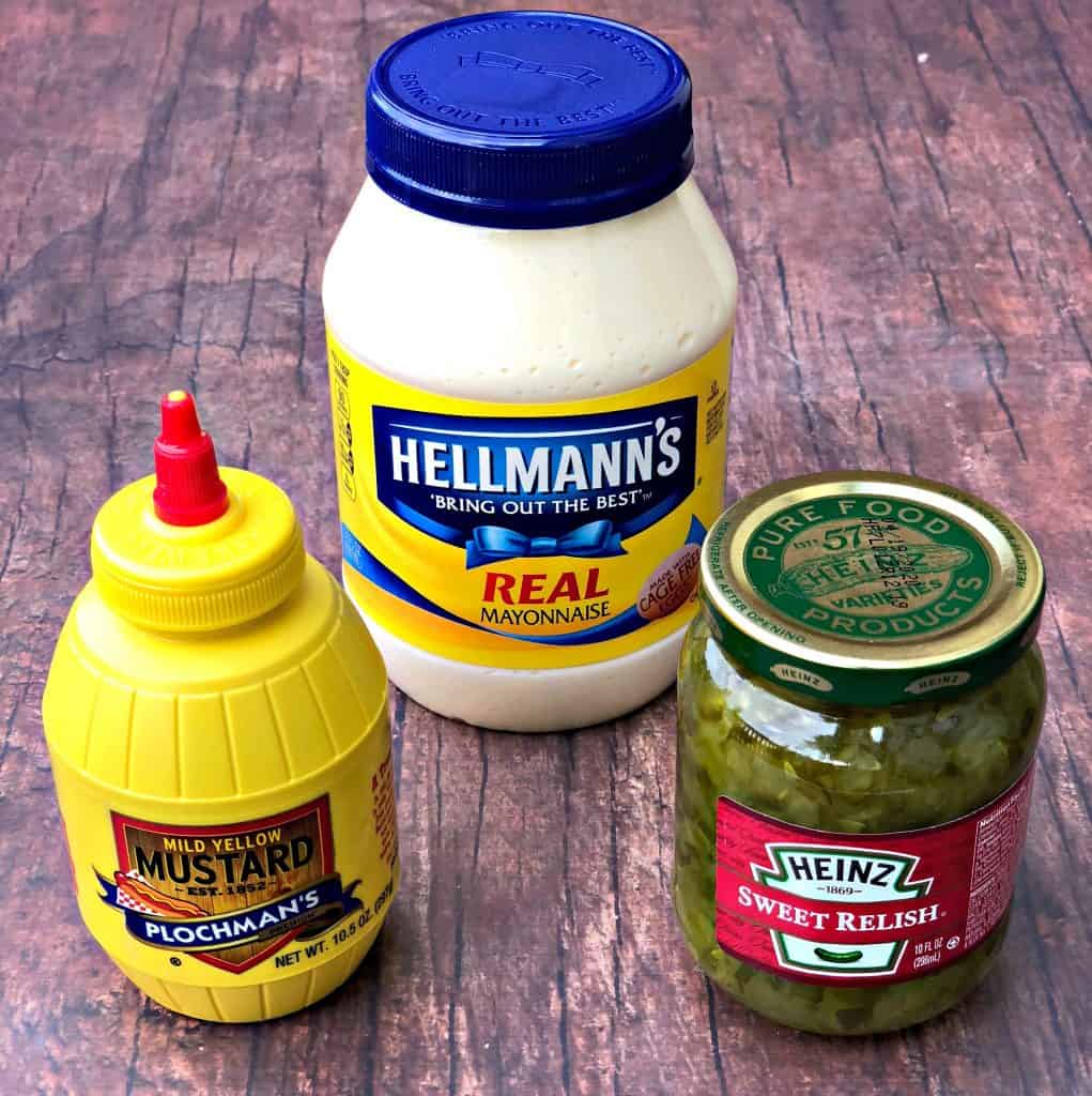 mayo, mustard, and relish in jars on a brown surface