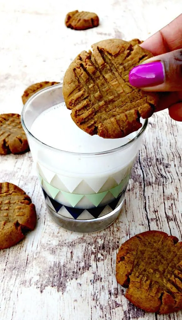 keto peanut butter cookies on a flat surface being dipped in a cup of milk