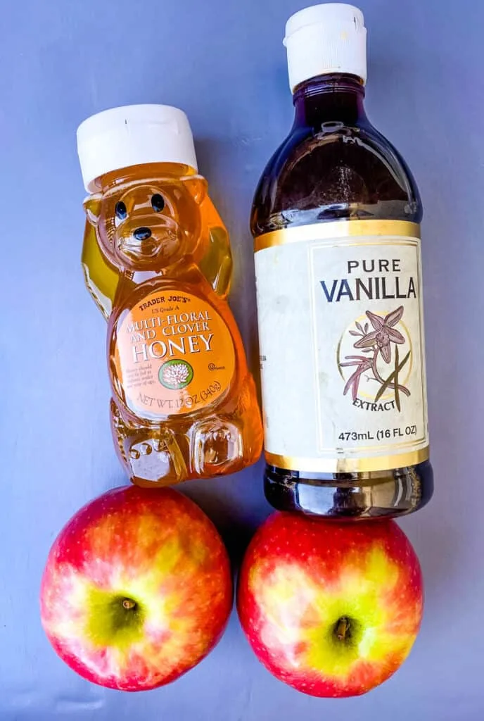 a bottle of honey, a bottle of vanilla, and fresh apples
