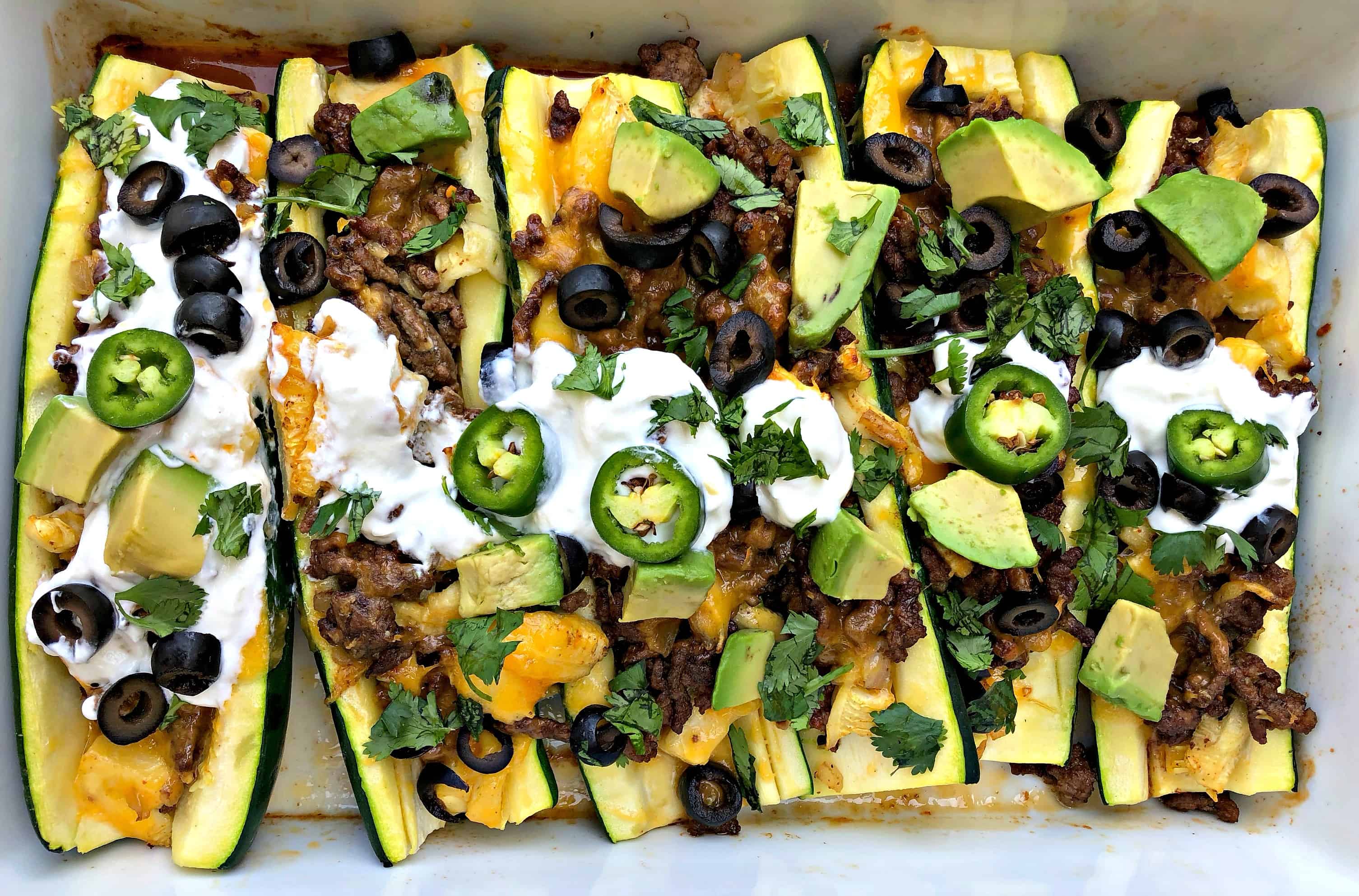 zucchini nachos with olives and sour cream in a baking dish