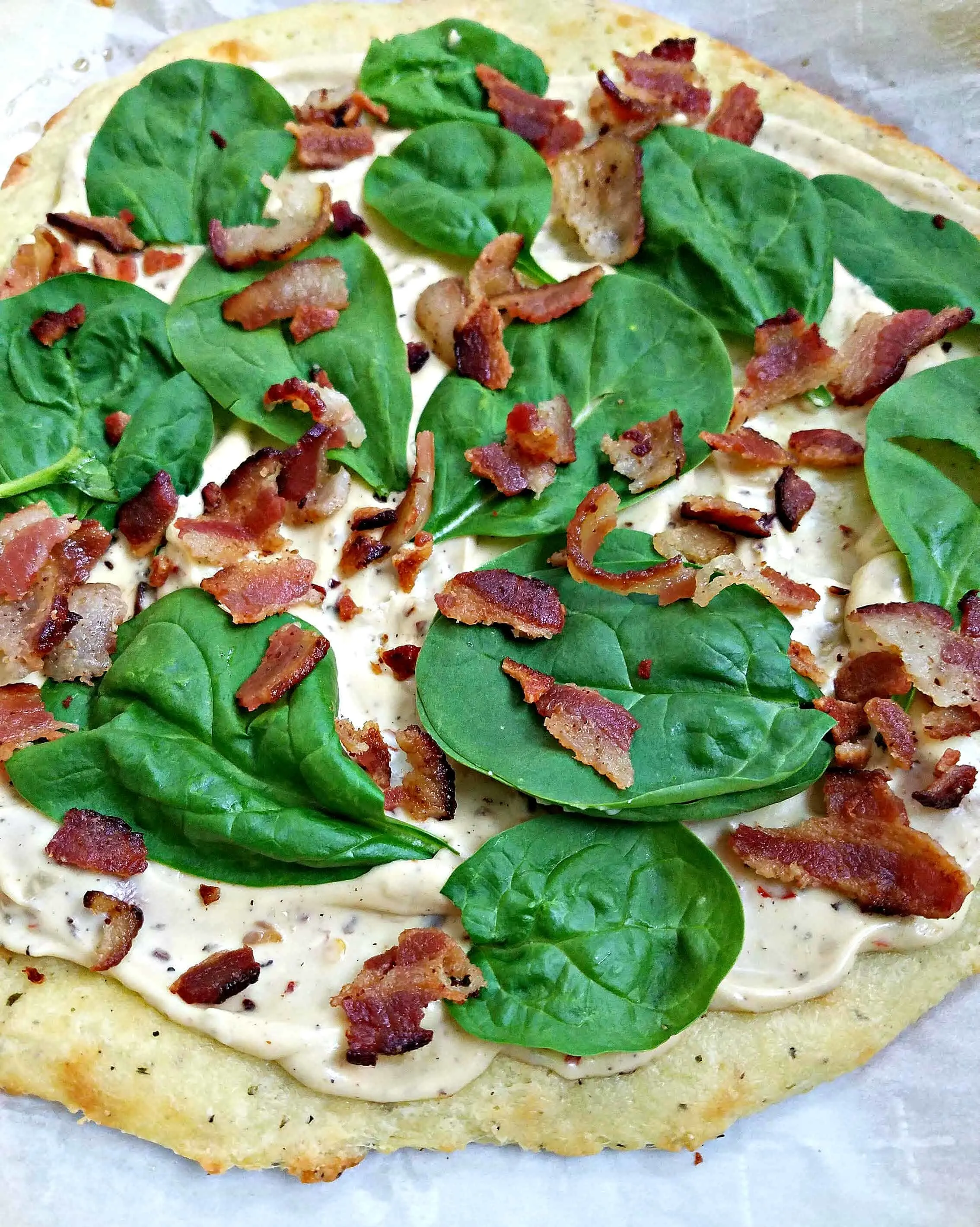 uncooked pizza with spinach and bacon