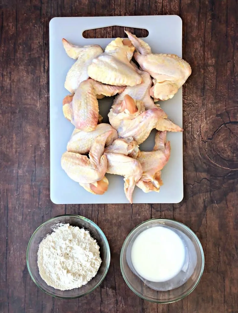 raw chicken wings on a cutting board with buttermilk and flour