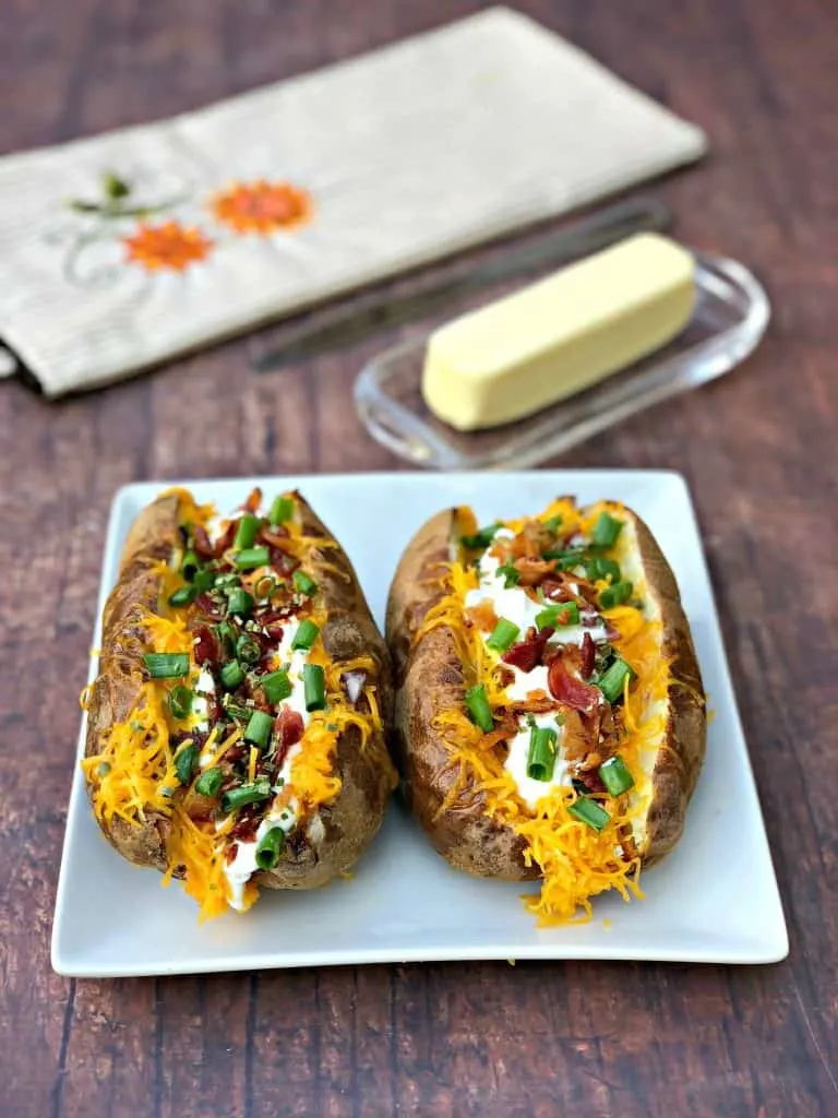 Easy, Air Fryer Loaded Stuffed Baked Potatoes is a quick recipe that will show you the time and how long to cook potatoes in the air fryer. These potatoes are stuffed with melted butter, sour cream, crunchy bacon, green onions, and chives. You can even prepare them as twice baked potatoes! air fryer loaded baked potato on a plate with butter