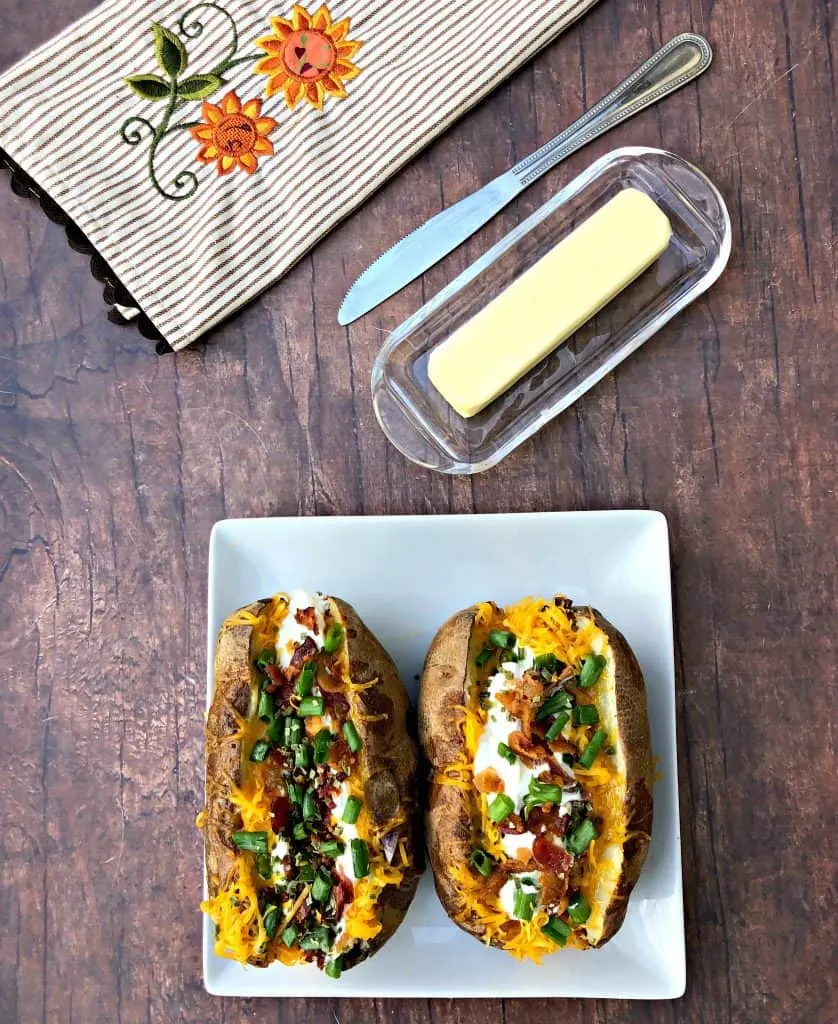 Easy, Air Fryer Loaded Stuffed Baked Potatoes is a quick recipe that will show you the time and how long to cook potatoes in the air fryer. These potatoes are stuffed with melted butter, sour cream, crunchy bacon, green onions, and chives. You can even prepare them as twice baked potatoes! air fryer loaded baked potato on a plate with butter