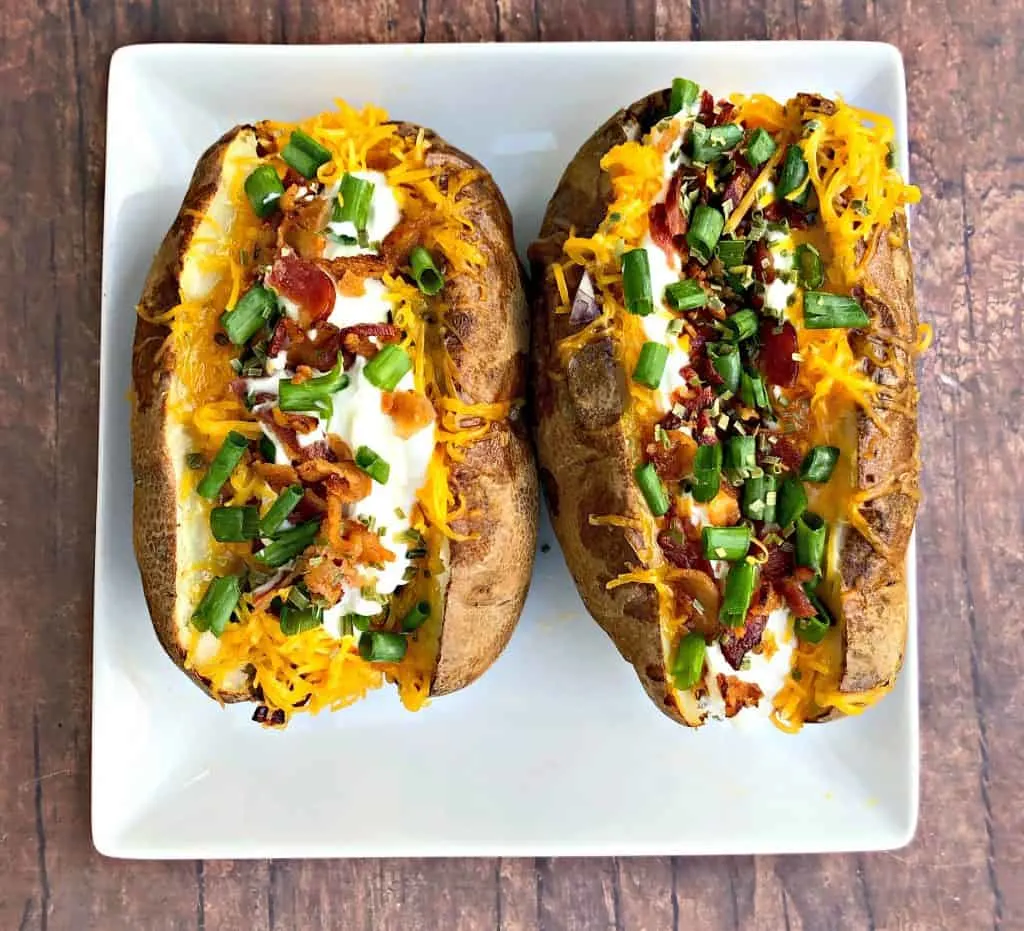 Easy, Air Fryer Loaded Stuffed Baked Potatoes is a quick recipe that will show you the time and how long to cook potatoes in the air fryer. These potatoes are stuffed with melted butter, sour cream, crunchy bacon, green onions, and chives. You can even prepare them as twice baked potatoes! air fryer loaded baked potato on a plate