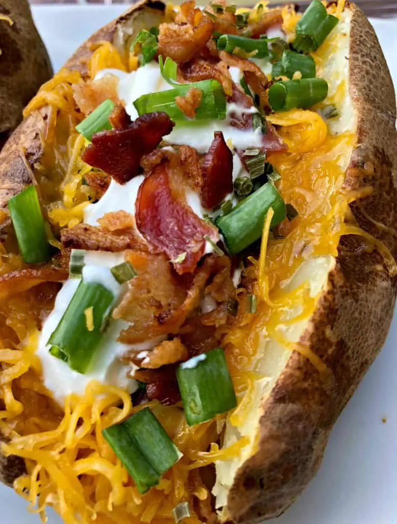 Easy, Air Fryer Loaded Stuffed Baked Potatoes is a quick recipe that will show you the time and how long to cook potatoes in the air fryer. These potatoes are stuffed with melted butter, sour cream, crunchy bacon, green onions, and chives. You can even prepare them as twice baked potatoes! air fryer loaded baked potato on a plate