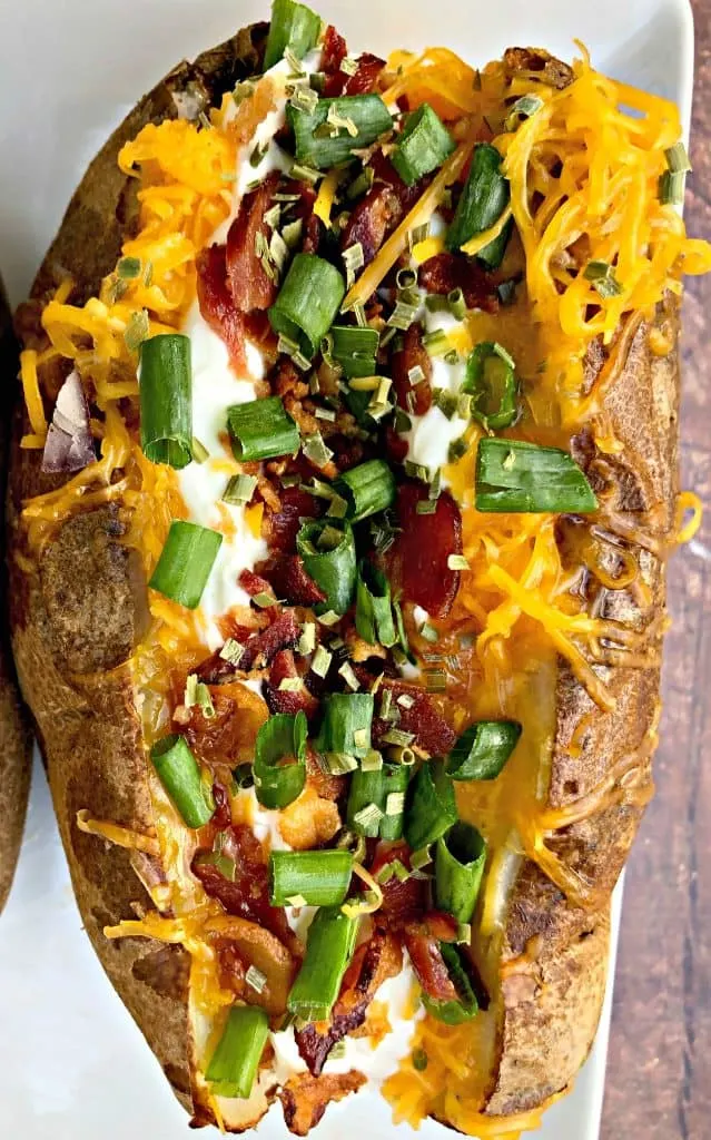 Easy, Air Fryer Loaded Stuffed Baked Potatoes is a quick recipe that will show you the time and how long to cook potatoes in the air fryer. These potatoes are stuffed with melted butter, sour cream, crunchy bacon, green onions, and chives. You can even prepare them as twice baked potatoes! air fryer loaded baked potato on a plate