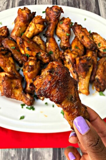 person holding air fryer buffalo chicken wing over a white plate of wings