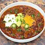 instant pot chili with shredded cheese, avocado, sour cream and jalapeno served in a white bowl