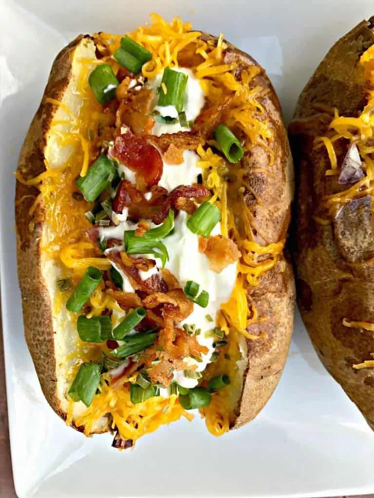 Easy, Air Fryer Loaded Stuffed Baked Potatoes is a quick recipe that will show you the time and how long to cook potatoes in the air fryer. These potatoes are stuffed with melted butter, sour cream, crunchy bacon, green onions, and chives. You can even prepare them as twice baked potatoes! air fryer loaded baked potato on white plate