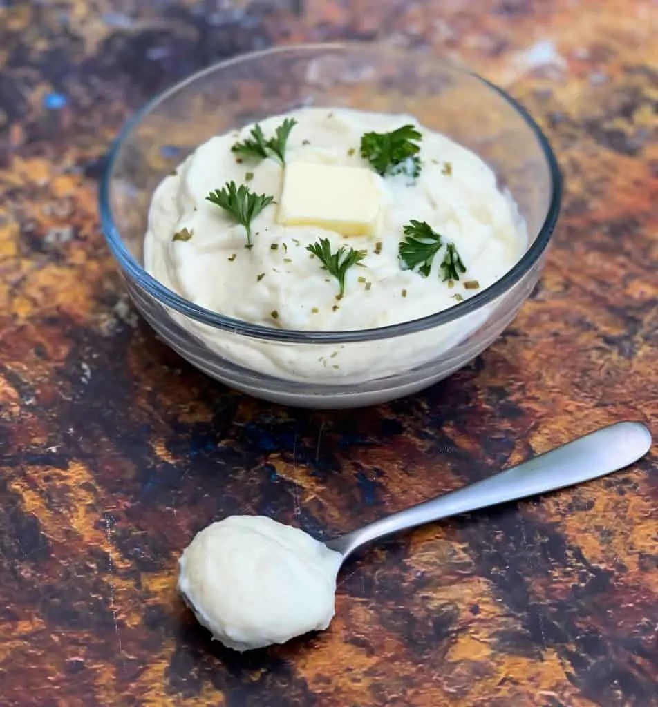 keto cauliflower mash in a glass bowl with butter, parsley, and a spoon