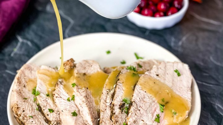 cooked turkey breasts with gravy on a white serving plate with fall decor in the background