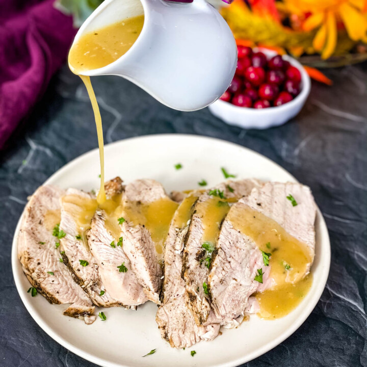 cooked turkey breasts with gravy on a white serving plate with fall decor in the background