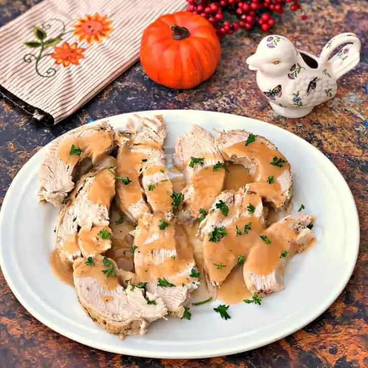 cooked turkey breasts with gravy on a white serving plate with fall decor in the background