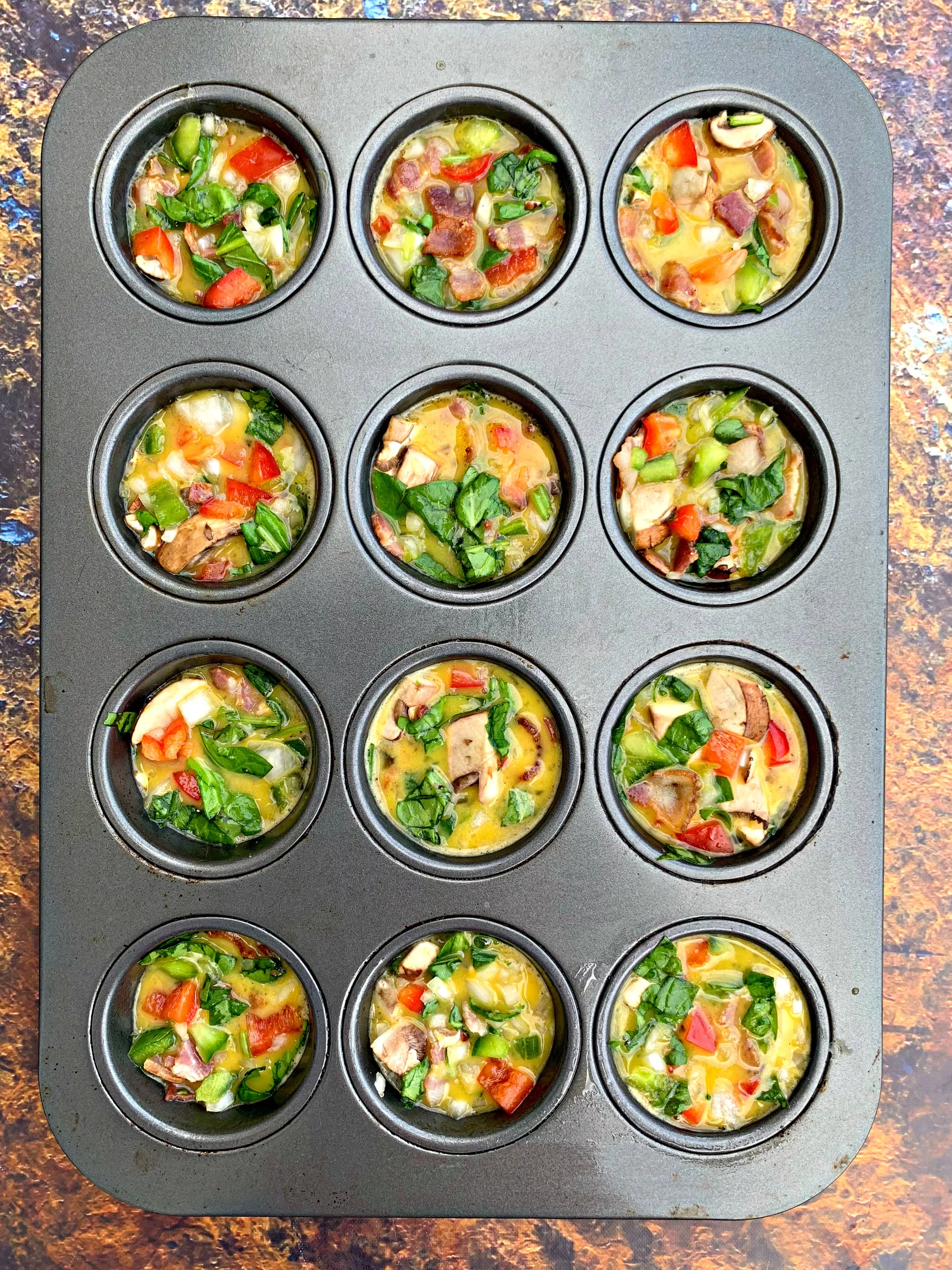 raw eggs with vegetables in a muffin tin
