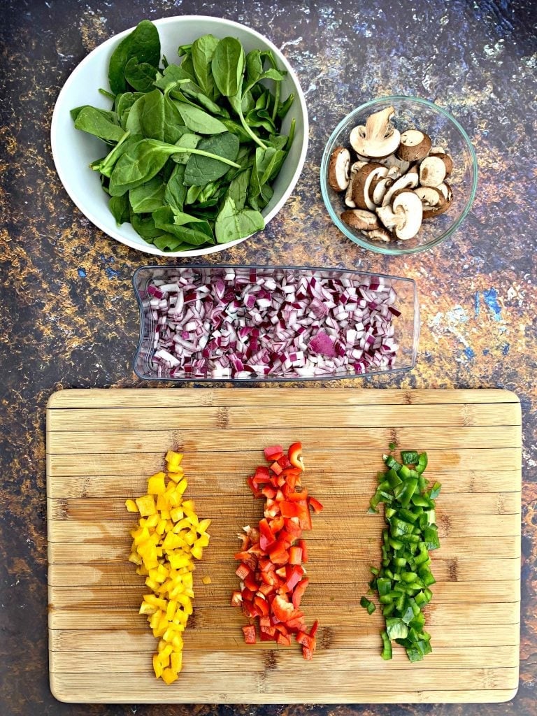 chopped veggies on a cutting board with onions, spinach, and mushrooms in a bowl