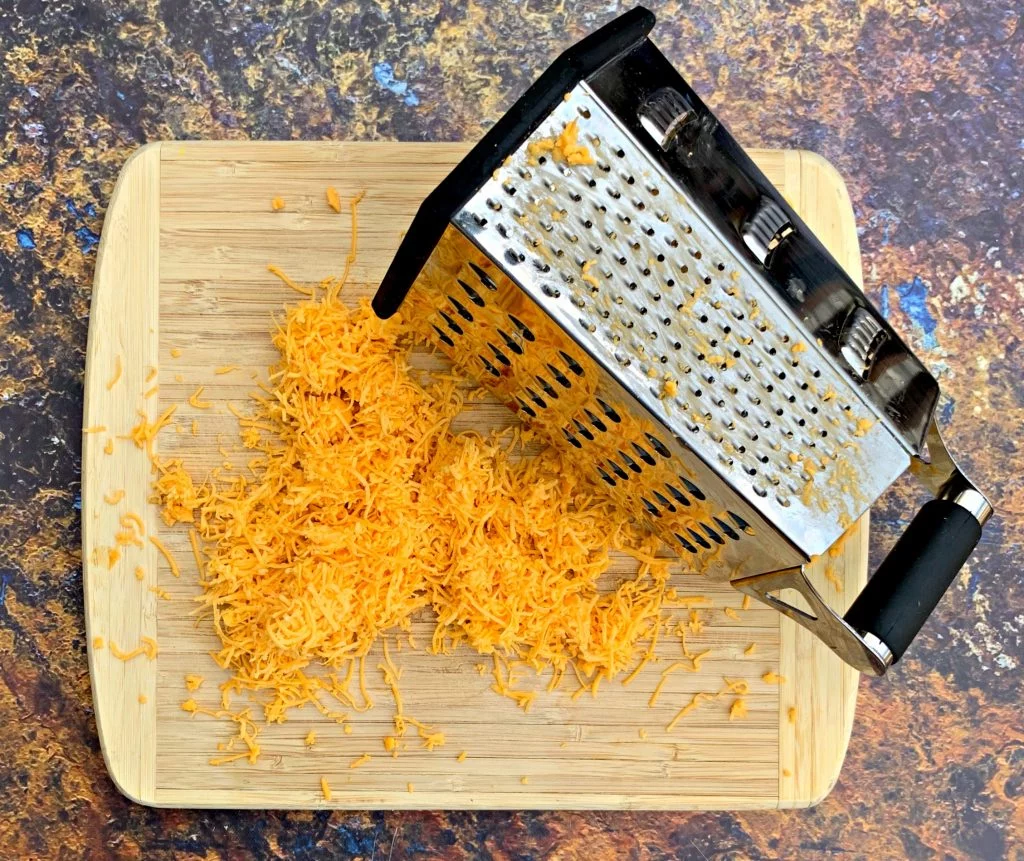 shredded cheddar on a cutting board with a grater
