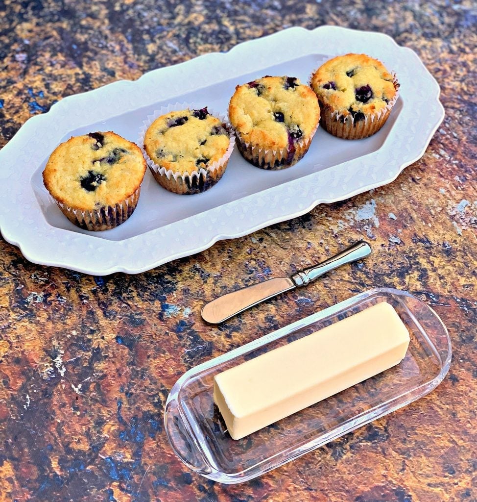 keto blueberry muffins on a white plate with a butter dish and a muffin tin with muffins