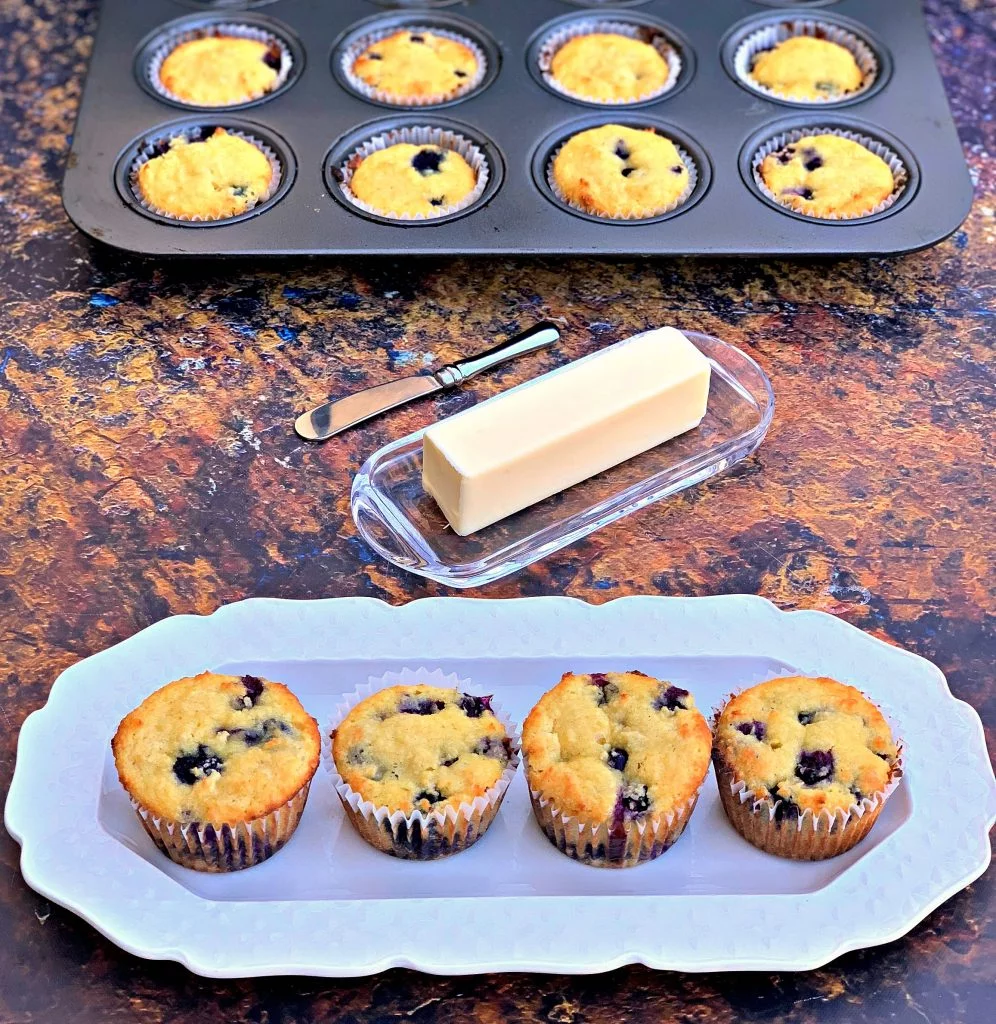 keto blueberry muffins on a white plate with a butter dish and a muffin tin with muffins