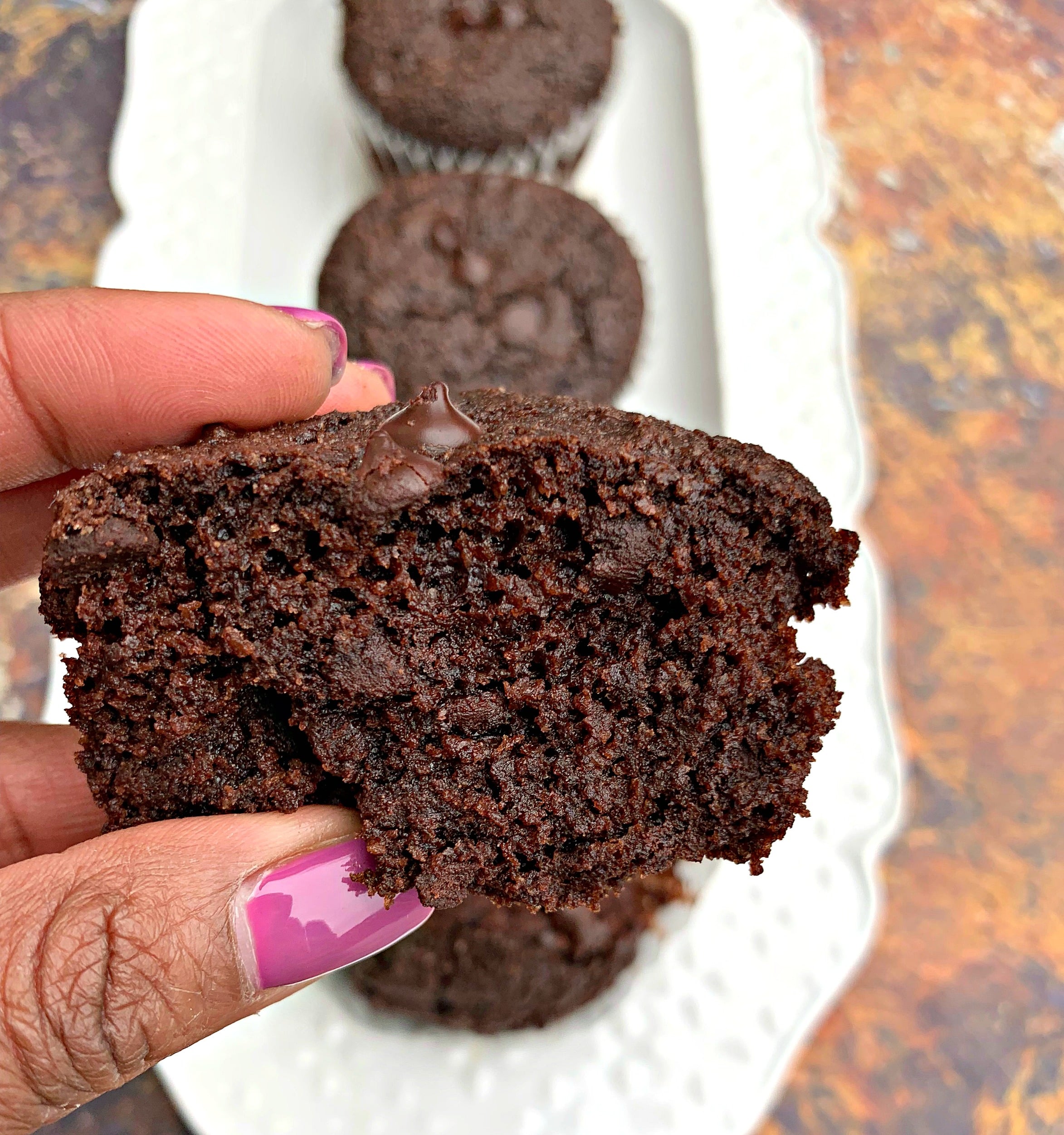 person holding keto low carb chocolate muffins over muffins on a white plate