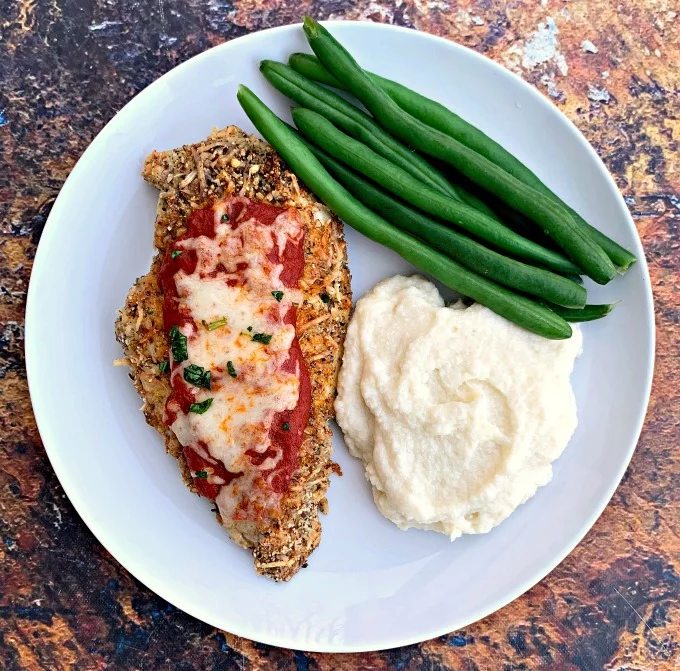 keto chicken parmesan with cauliflower mash and green beans on a white plate