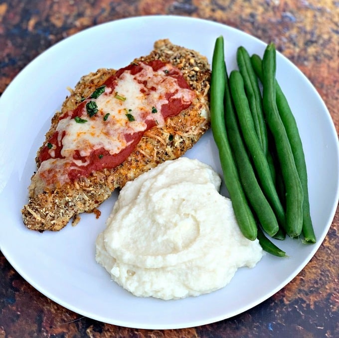 keto chicken parmesan with cauliflower mash and green beans on a white plate