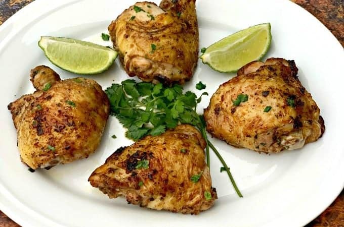 air fryer keto low carb cilantro lime chicken thighs on a white plate with lime and fresh cilantro