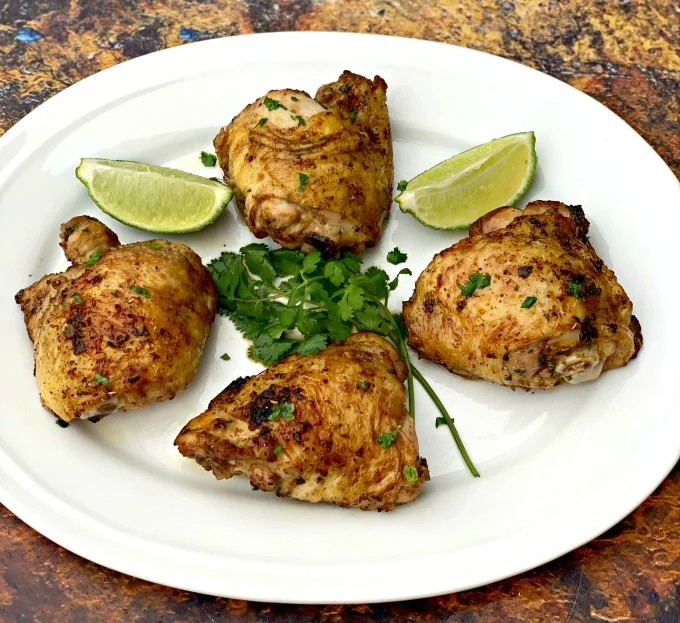 air fryer keto low carb cilantro lime chicken thighs on a white plate with lime and fresh cilantro