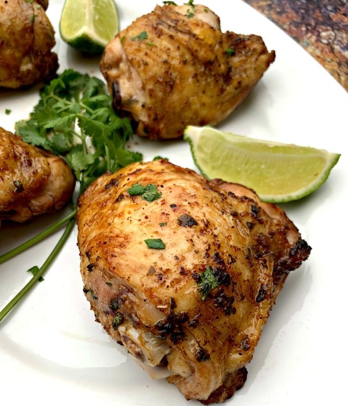 air fryer keto low carb cilantro lime chicken thighs on a white plate with lime and fresh cilantro