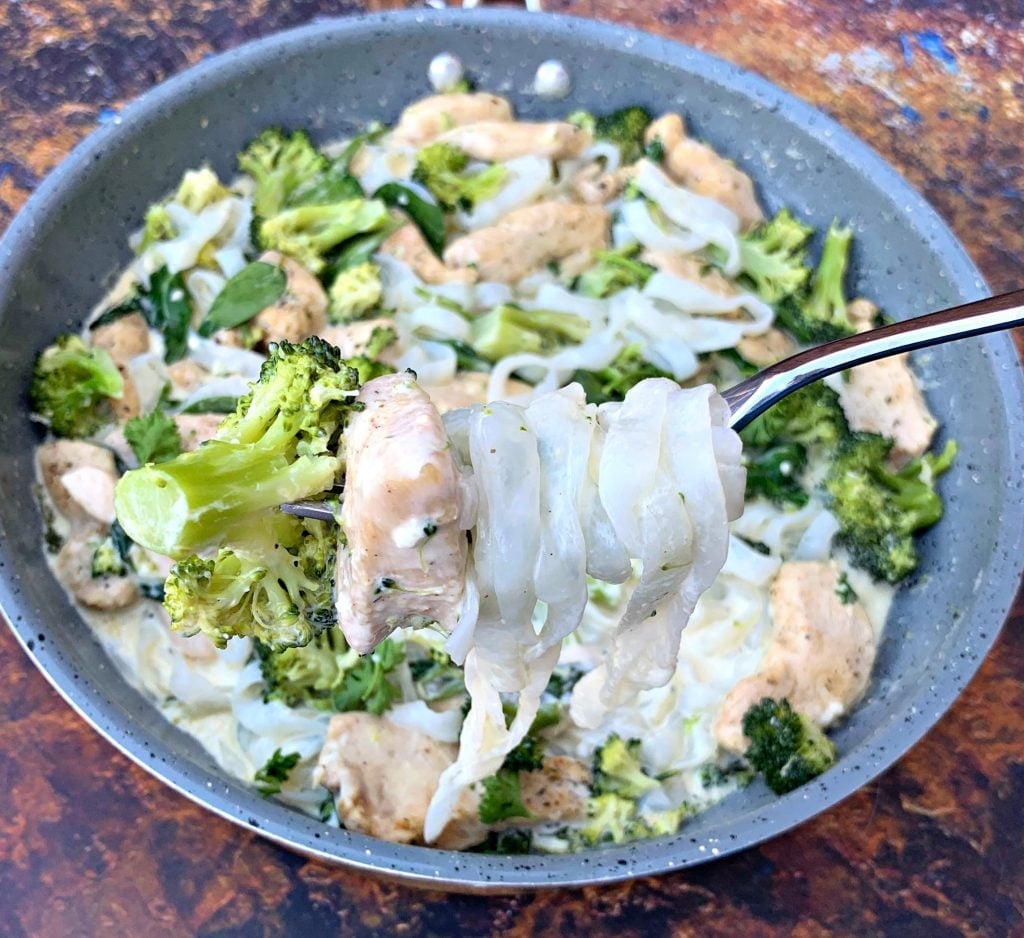 person holding keto chicken alfredo with broccoli and spinach in a skillet with a fork