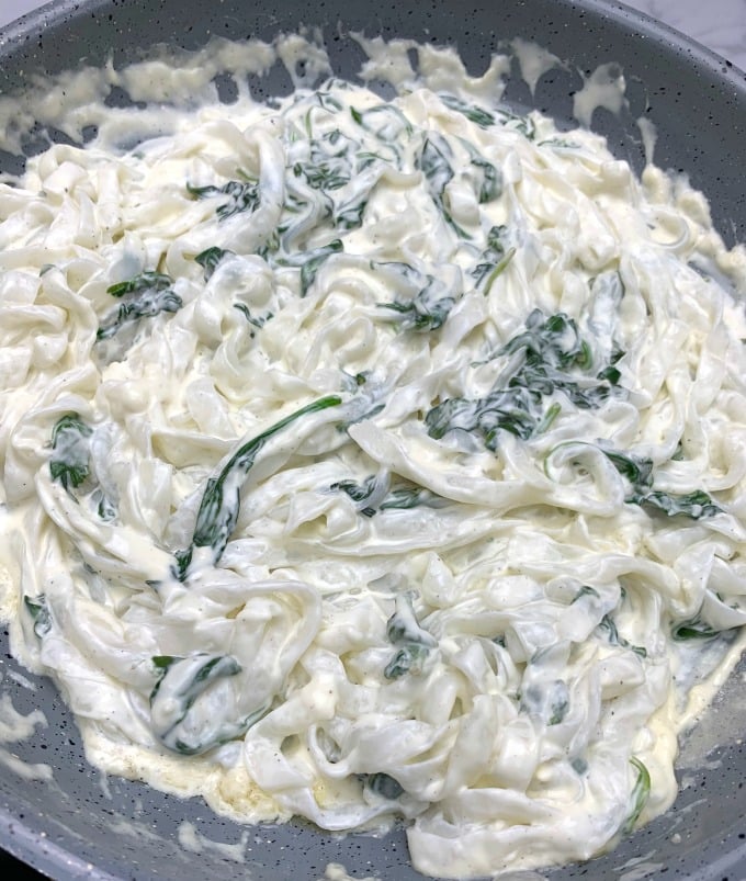 cooked miracle noodles and keto chicken alfredo with broccoli and spinach in a skillet