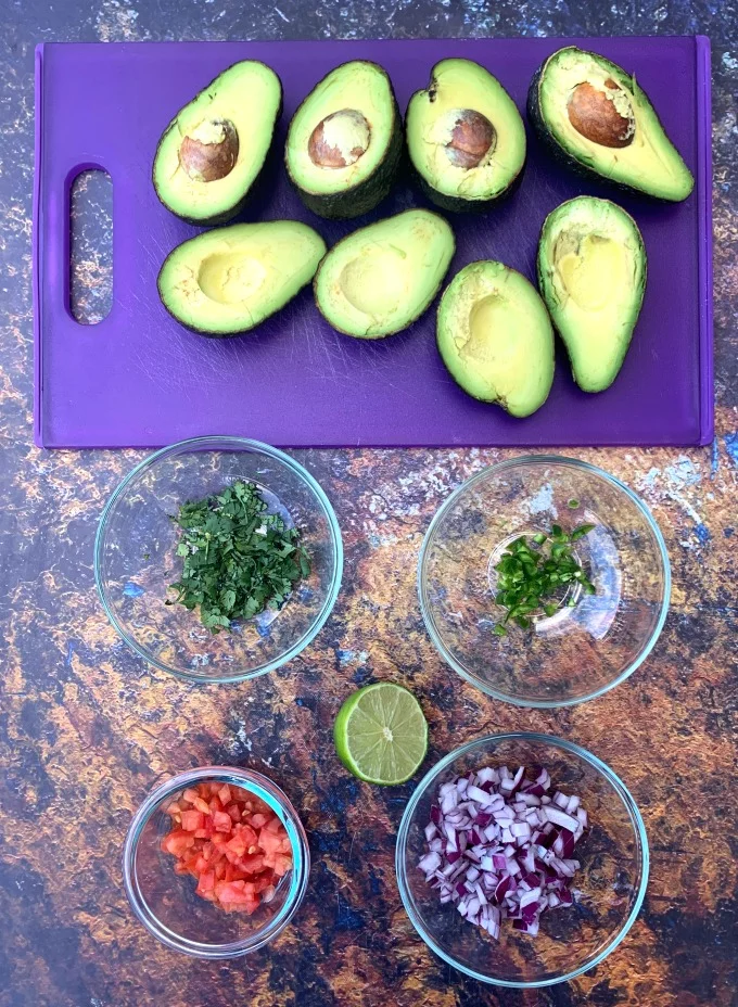 ingredients for keto guacamole avocado, cilantro, tomatoes, and lime in bowls