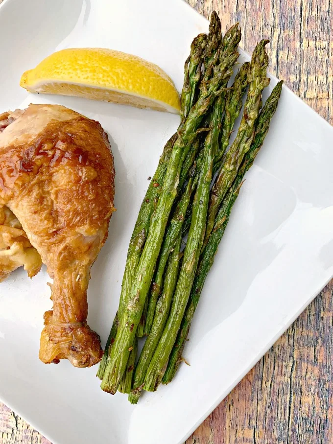 air fryer roasted asparagus on a white plate with lemon with chicken