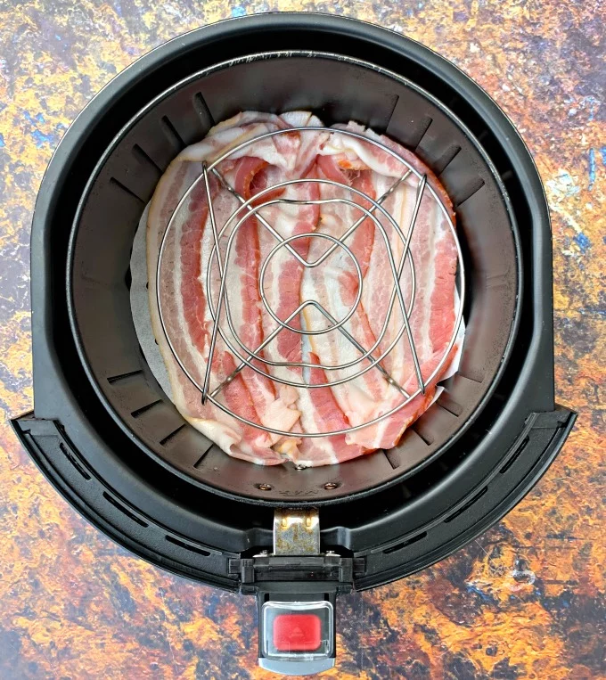 uncooked bacon in an air fryer on parchment paper