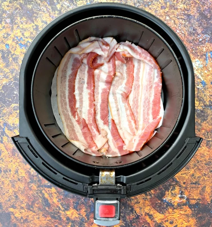 uncooked bacon in an air fryer on parchment paper