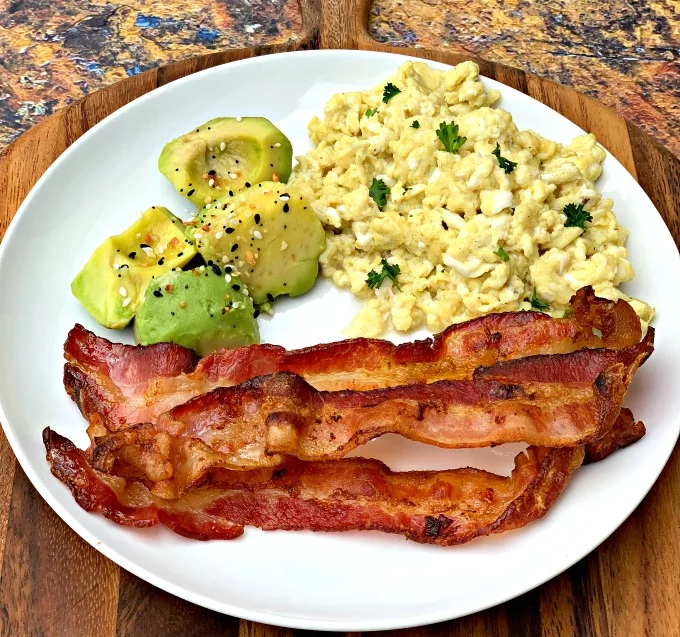 cooked air fryer bacon on a white plate with eggs and avocado