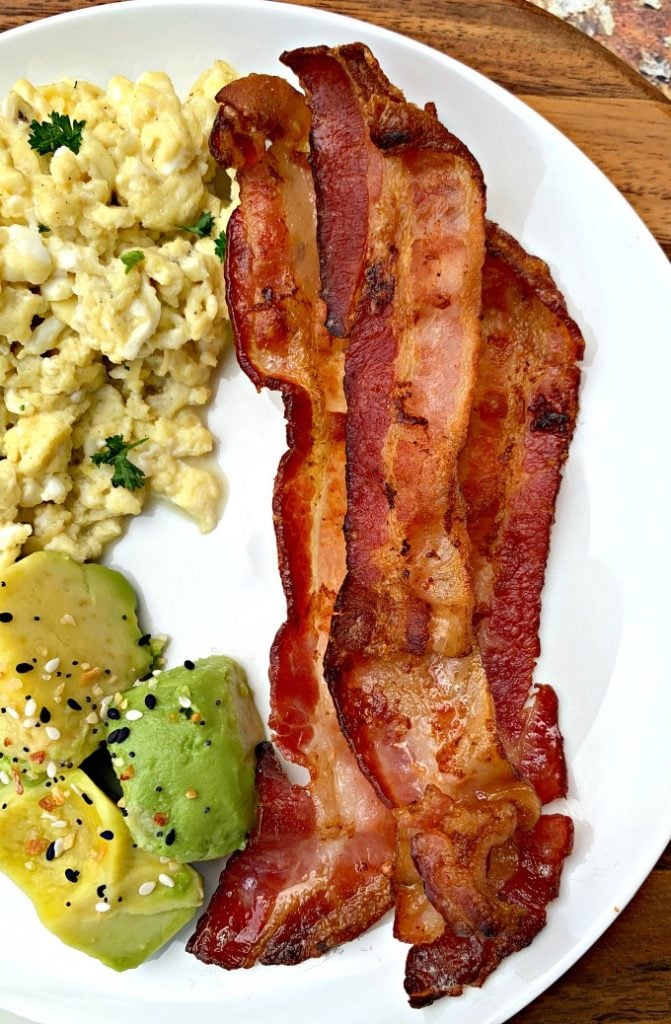 cooked air fryer bacon on a white plate with eggs and avocado