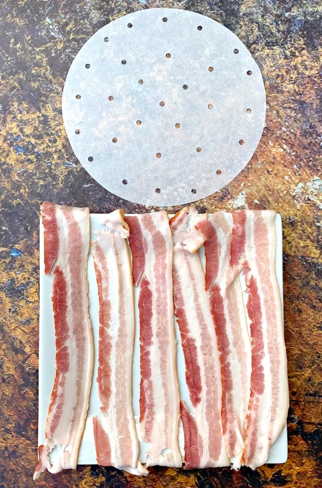 air fryer parchment paper and uncooked bacon on a white plate
