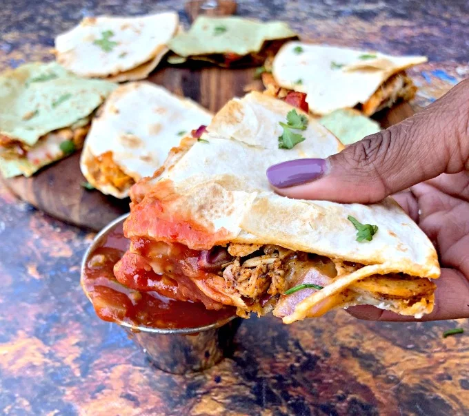 person holding air fryer chicken quesadillas dipped in salsa