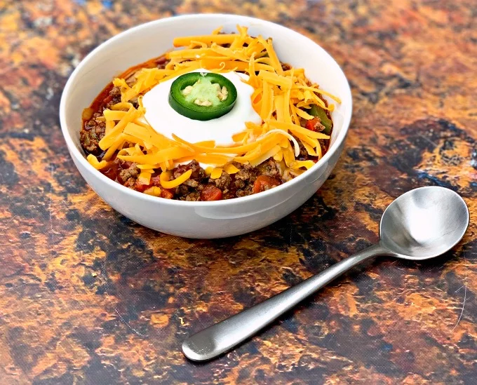 keto beef chili with shredded cheese in a white bowl with shredded cheese and sour cream