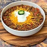 keto beef chili with shredded cheese in a white bowl with shredded cheese and sour creama