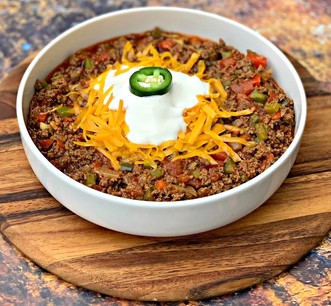 keto beef chili with shredded cheese in a white bowl with shredded cheese and sour creama