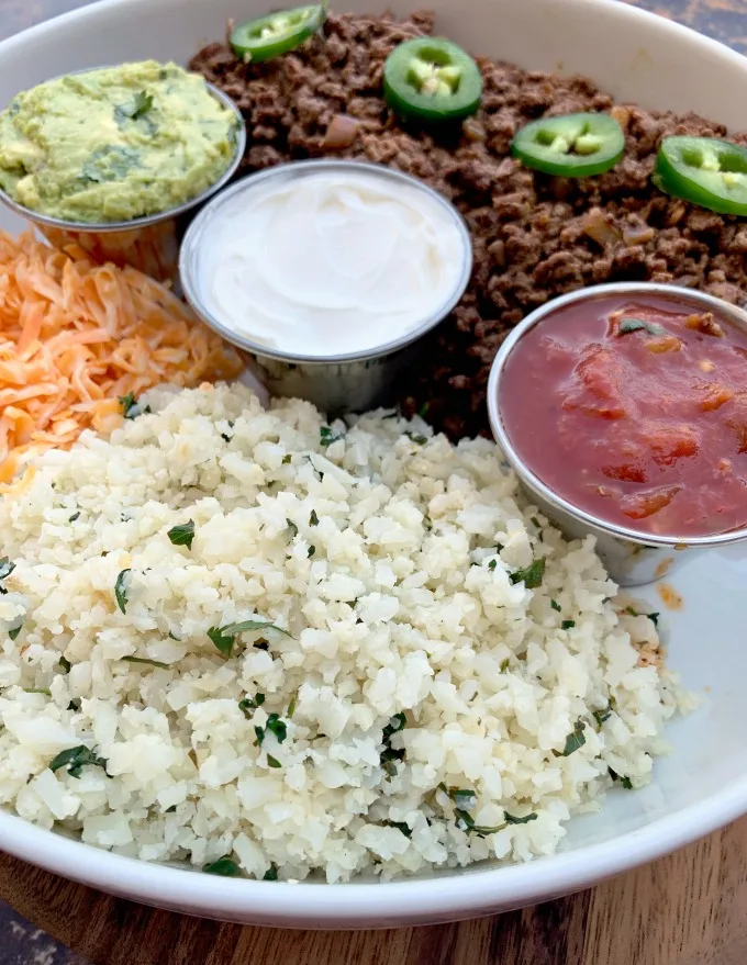 cilantro lime cauliflower rice in a white bowl with salsa, sour cream, and guacamole