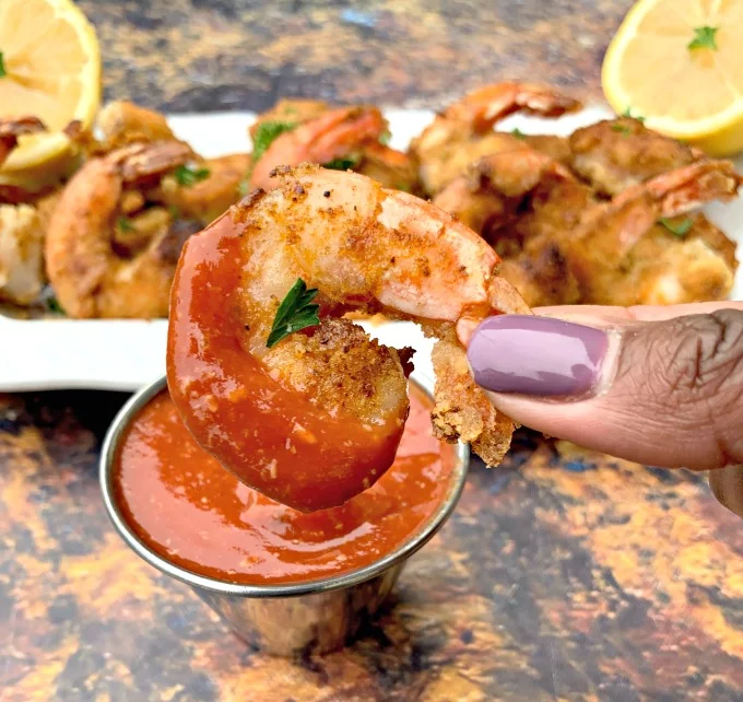 person holding keto low carb breaded shrimp dipped in cocktail sauce