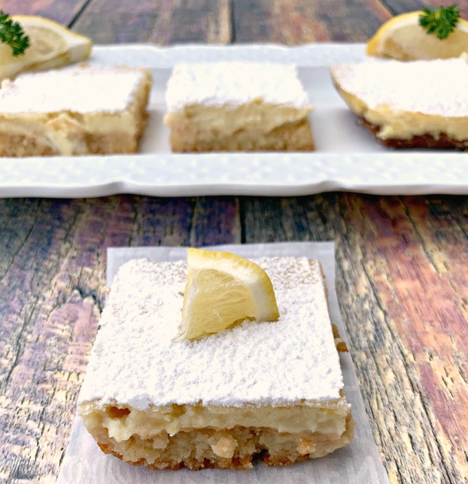 keto lemon bar on parchment paper that has been bitten with 2 lemons