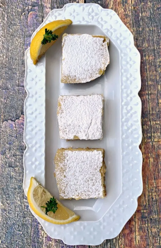 3 keto lemon bars on a white plate topped with confectioner's sugar