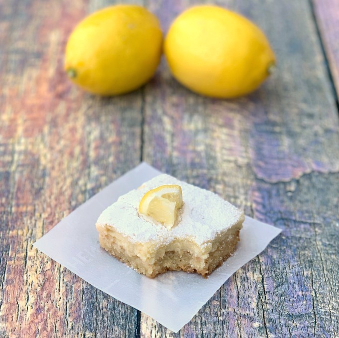 keto lemon bar on parchment paper that has been bitten with 2 lemons